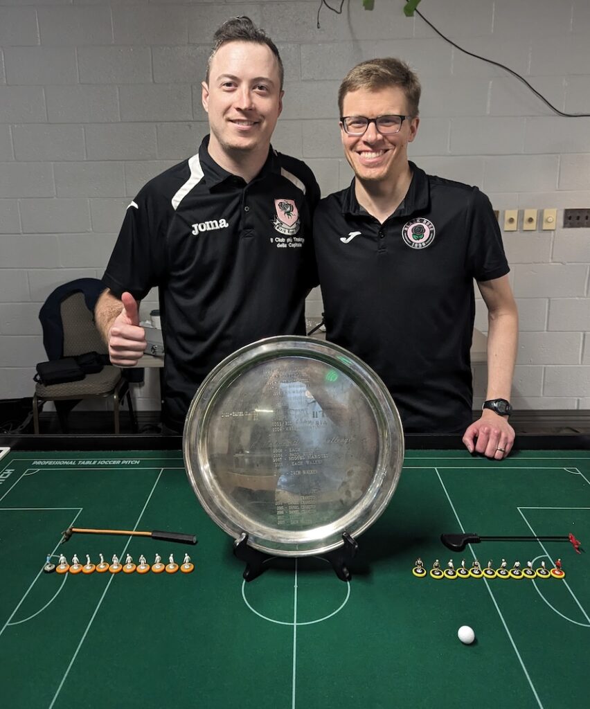 Two men standing near a table soccer table with a trophy