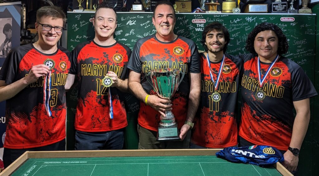 Five men standing in red and black sports uniforms with a trophy